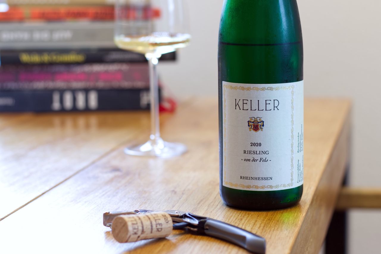 Eine Flasche Riesling Von der Fels vom Weingut Keller auf einem Holztisch. Im Hintergrund sind ein Weinglas und Bücherstapel zu sehen. Vor den Flaschen liegt der Korken der Flasche am Kellnermesser.